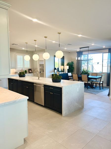 A bright, elegant kitchen with a large marble island, black cabinetry, and gold pendant lighting.