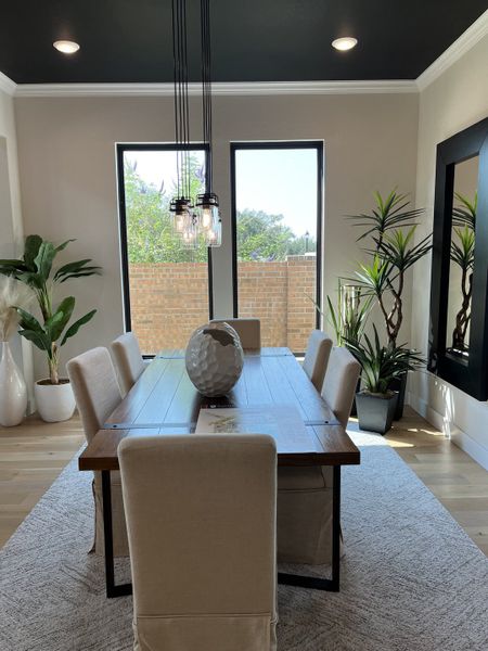 A chic dining room with a wooden table, upholstered chairs, modern pendant lighting, and lush greenery accents.