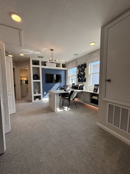 A bright and modern study nook with built-in shelving, a cozy workspace, and elegant lighting in Eden at Crossprairie by M/I Homes (St. Cloud, FL).

