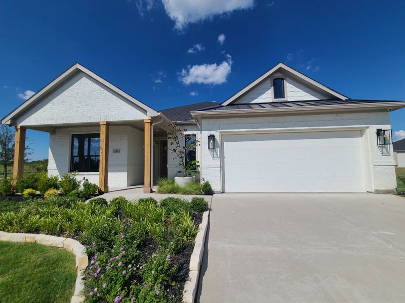 A sleek white brick home with wooden accents and lush landscaping in University Park at Northpointe by Wyndham Custom Homes (Denton, TX).