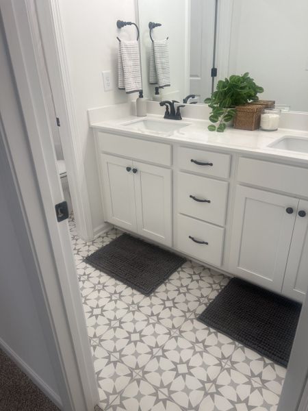 A chic bathroom with patterned tile flooring, dual sinks, sleek black fixtures, and elegant white cabinetry. A chic bathroom with patterned tile flooring, dual sinks, sleek black fixtures, and elegant white cabinetry.