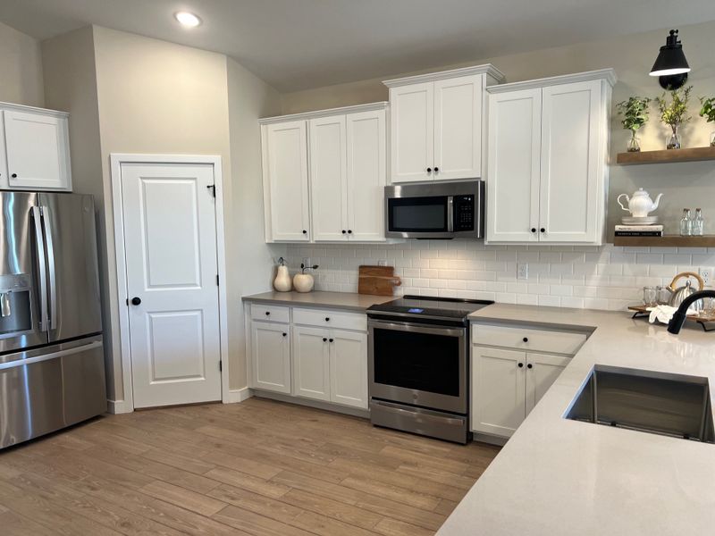 A modern kitchen with white cabinetry, stainless steel appliances, and wooden floors, accented by elegant open shelving.