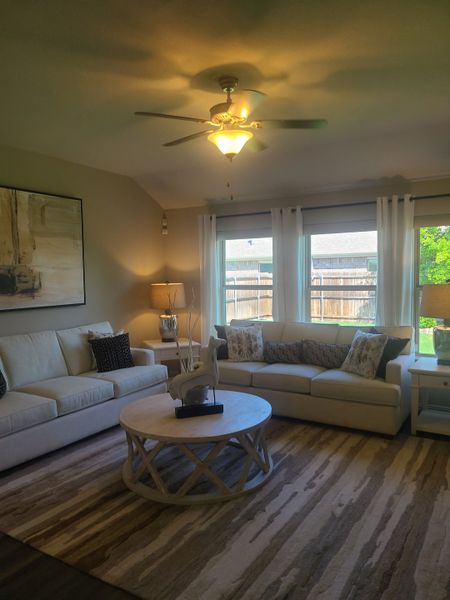 A cozy living room featuring cream sofas, a round coffee table, and elegant decor with natural light streaming through windows.