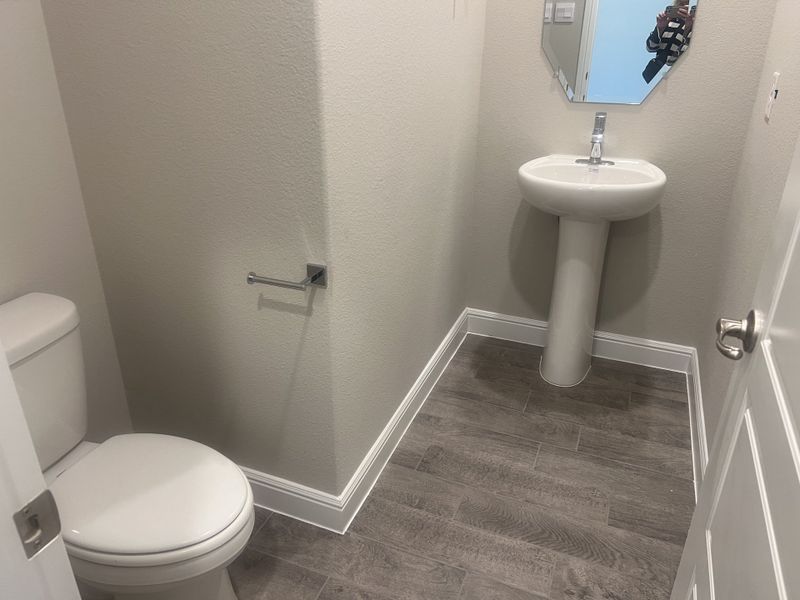 A compact powder room with a pedestal sink, modern fixtures, and wood-patterned flooring. A compact powder room with a pedestal sink, modern fixtures, and wood-patterned flooring.