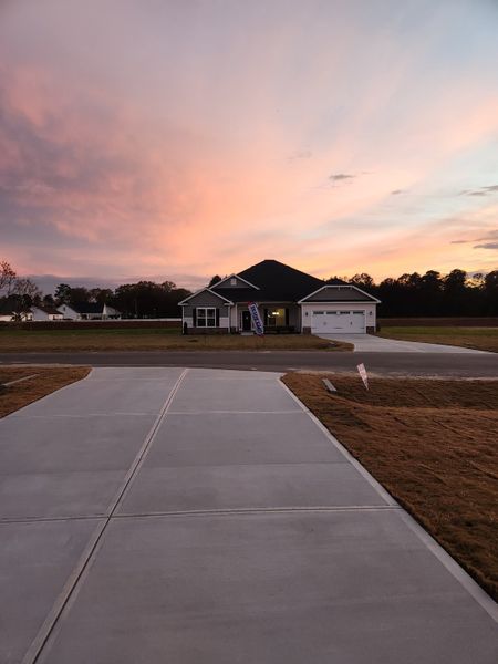 A charming home with a wide driveway and sunset backdrop in Cool Water by Adams Homes (Bailey, NC).