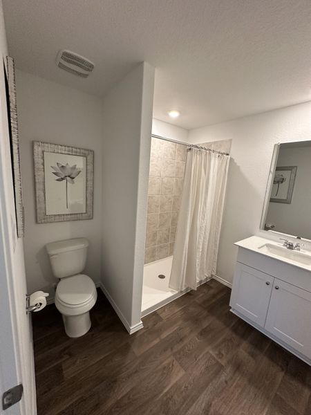 A modern bathroom featuring wood-look flooring, a minimalist vanity, shower with tile accents, and stylish artwork.