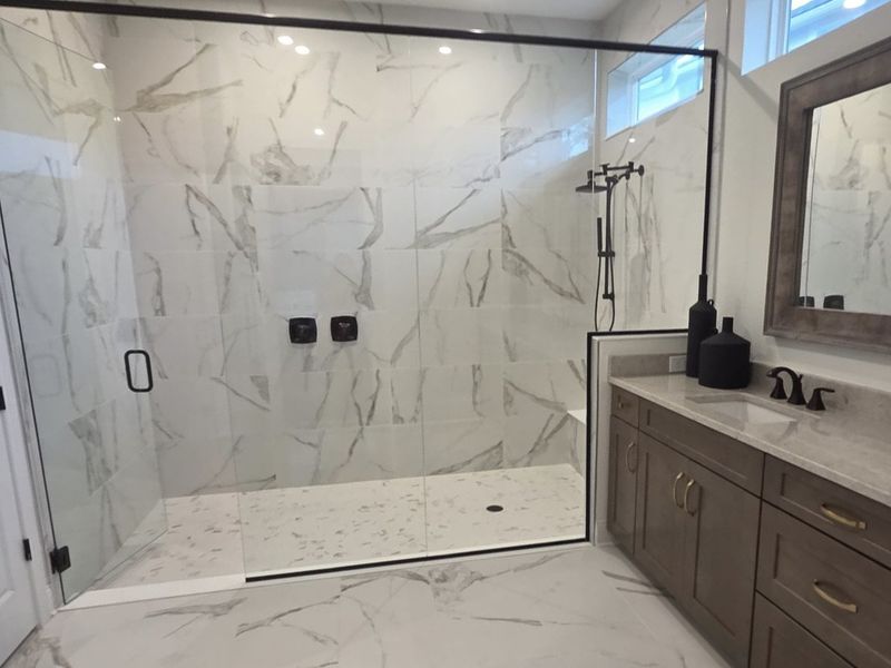 A luxurious bathroom featuring a spacious glass shower, marble tiles, and a sleek wooden vanity with modern fixtures.