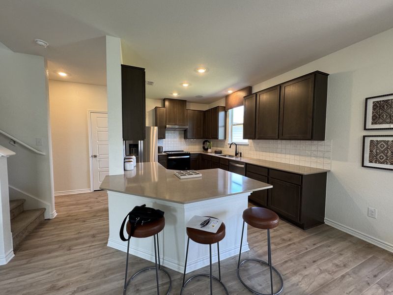 Modern kitchen with dark cabinets, light countertops, and a spacious island with barstools. Warm, inviting ambiance throughout. Modern kitchen with dark cabinets, light countertops, and a spacious island with barstools. Warm, inviting ambiance throughout.