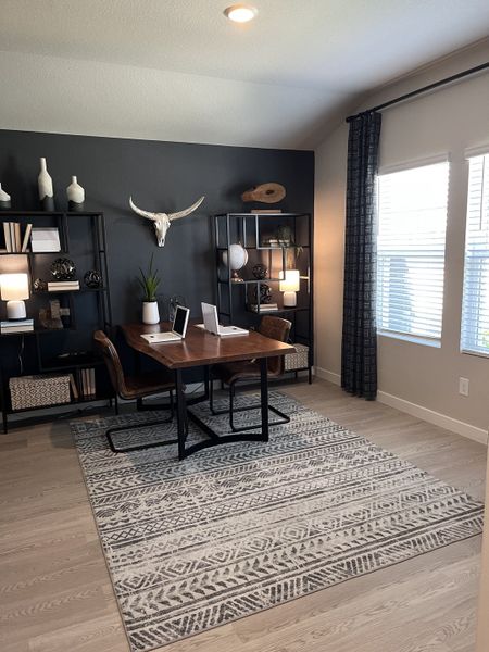 A stylish office with a wooden desk, modern rug, and open shelving, featuring decor with a contemporary touch.