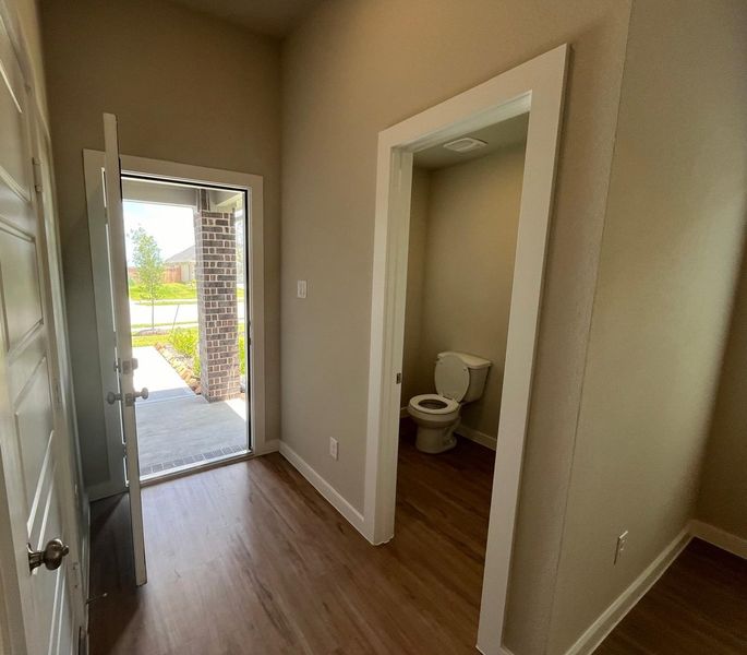 A cozy entryway with wood flooring leads to a half bath, featuring a simple design and natural light streaming in.