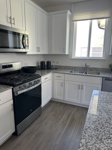 A modern kitchen with white cabinetry, granite countertops, stainless steel appliances, and wood flooring.
