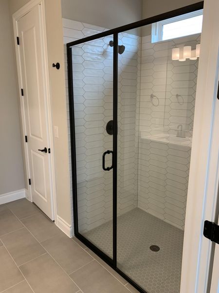 A sleek bathroom shower with geometric tiles, black trim, and a modern glass door.