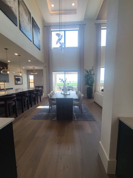 A sophisticated dining area with high ceilings, large windows, elegant chandelier, and a long table on a plush rug.