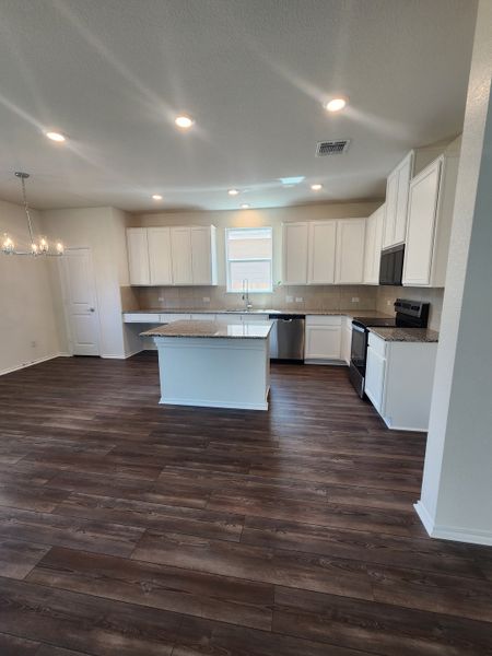 A modern kitchen featuring dark wood floors, white cabinets, granite countertops, and sleek lighting.