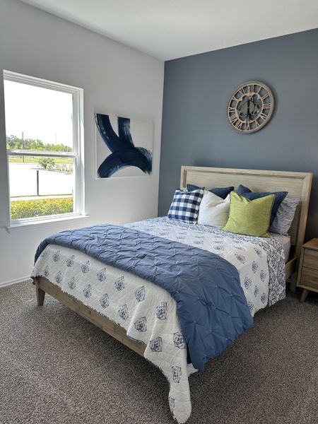 A cozy bedroom featuring a soft blue accent wall, stylish bedding, and elegant decor with a view through a large window.