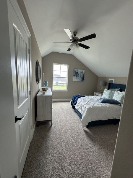A cozy bedroom with vaulted ceilings, soft carpeting, a ceiling fan, and bright natural light from a window. A cozy bedroom with vaulted ceilings, soft carpeting, a ceiling fan, and bright natural light from a window.