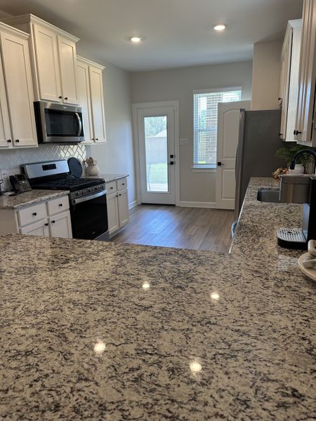 A modern kitchen with granite countertops, white cabinetry, and stainless steel appliances. Bright and airy ambiance.