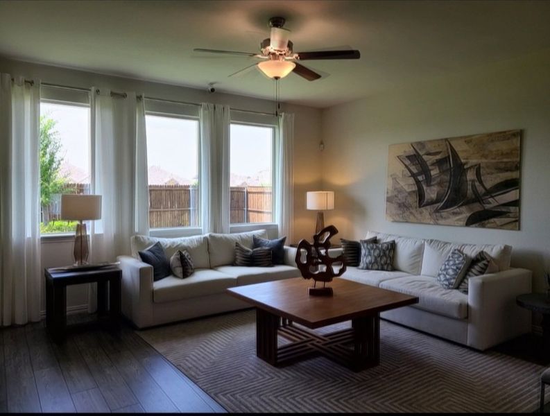 A cozy living room with white sofas, wooden table, art decor, and natural light filtering through sheer curtains.