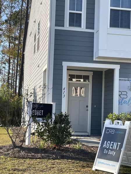 A modern blue townhome with white trim and a manicured yard in Boykins Run Townhomes by DRB Homes (Moncks Corner, SC).
