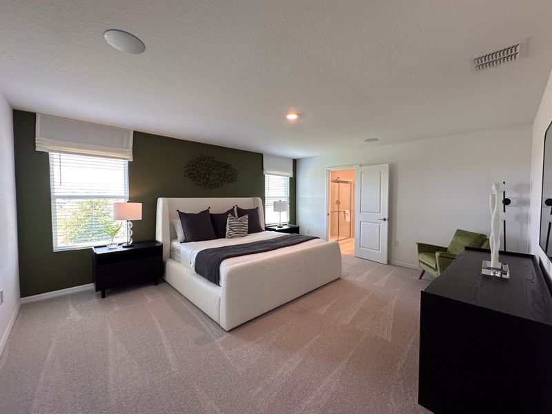 A cozy bedroom with plush carpeting, a stylish upholstered bed, green accent wall, and modern decor elements.