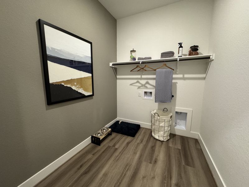 A sleek laundry room with a stylish abstract painting, wooden flooring, and a convenient shelving area.