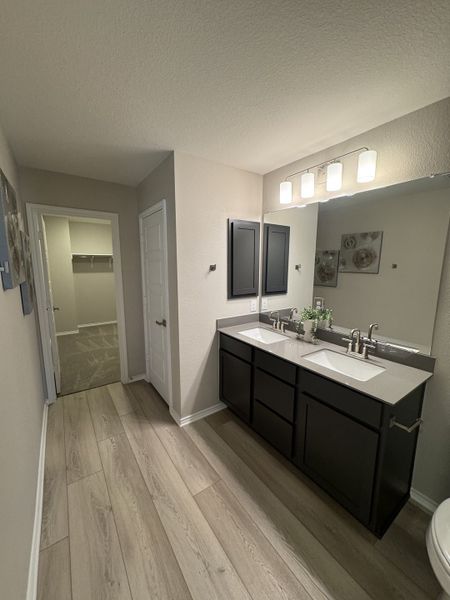A modern bathroom with dual sinks, sleek dark cabinetry, light wood flooring, and elegant lighting. A modern bathroom with dual sinks, sleek dark cabinetry, light wood flooring, and elegant lighting.