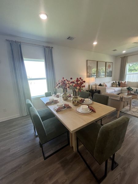 A modern dining area with a light wood table, plush green chairs, and elegant decor, flowing into a cozy living space.