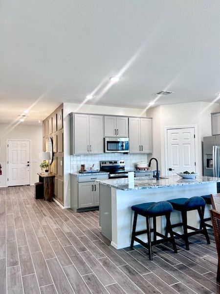 A modern kitchen with sleek gray cabinets, granite countertops, and stylish barstools on hardwood floors.