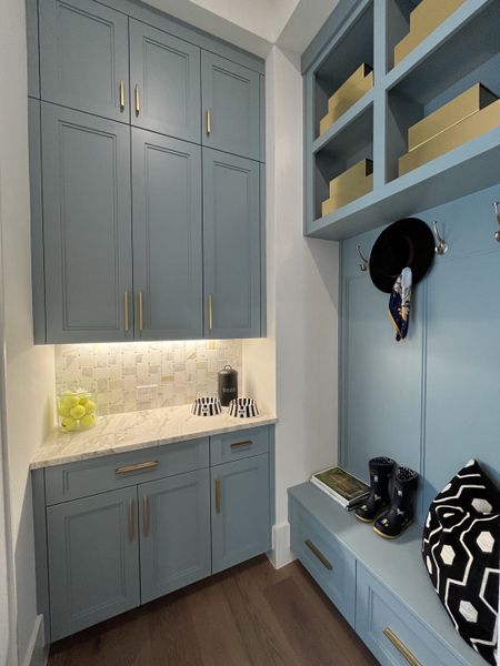 A chic mudroom with blue cabinetry, brass hardware, a marble countertop, and decorative accents.