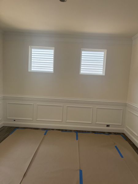 A bright, unfinished room with panel molding, two square windows, and covered flooring. A bright, unfinished room with panel molding, two square windows, and covered flooring.