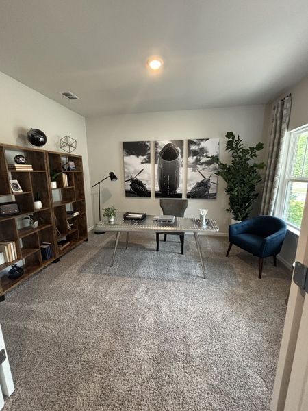 A modern office with a sleek desk, cozy blue chair, built-in shelves, and aviation-themed artwork.