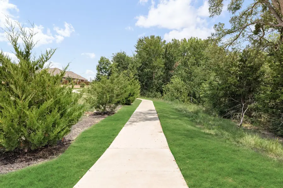 Concrete walking path through green lawn with trees and shrubs lining both sides of the trail