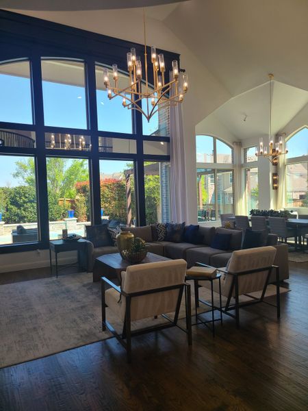 A modern living area with large windows, elegant chandeliers, and stylish seating, offering a bright and spacious ambiance.
