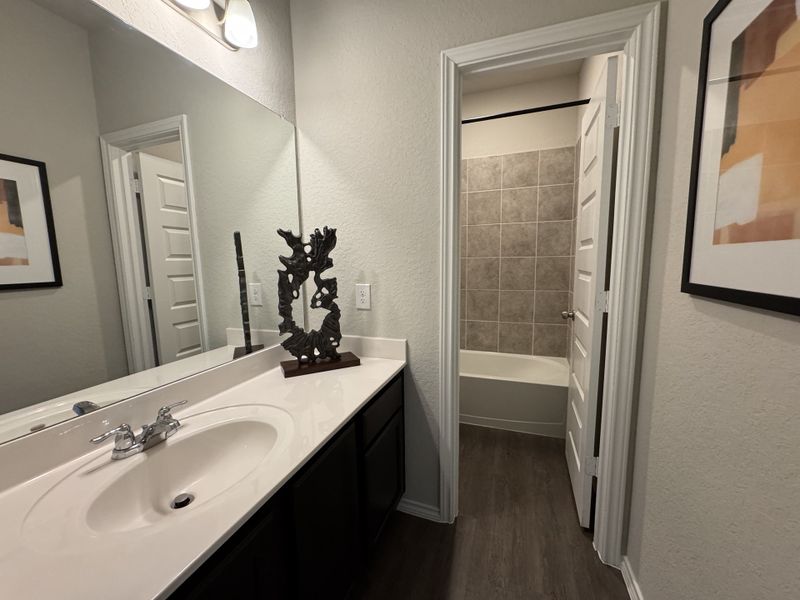 A modern bathroom featuring a sleek sink, large mirror, abstract decor, and a tiled bathtub, all elegantly designed.