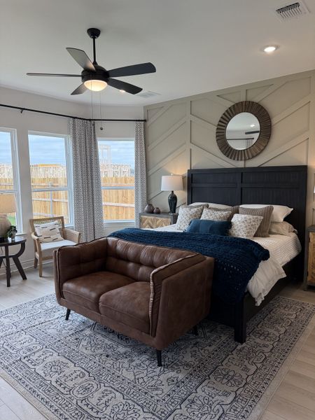 A cozy bedroom featuring a textured accent wall, stylish bedding, leather loveseat, and elegant decor.