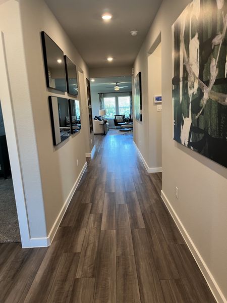 A sleek hallway featuring wood flooring, modern artwork, and recessed lighting leading to a cozy, light-filled living area.