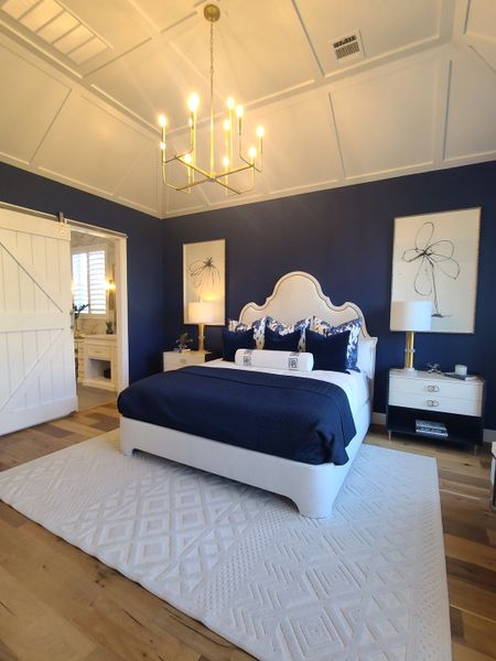 Elegant bedroom featuring navy walls, a chic gold chandelier, white bed frame, and modern accents.