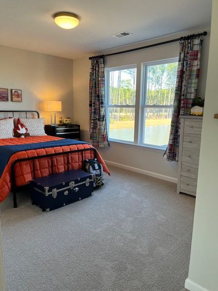 A cozy bedroom with a bright window, vibrant orange bedding, and plaid curtains, creating a welcoming and comfortable ambiance.
