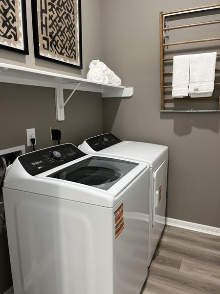 A modern laundry room with sleek appliances, wooden drying rack, artistic wall decor, and light wood flooring.