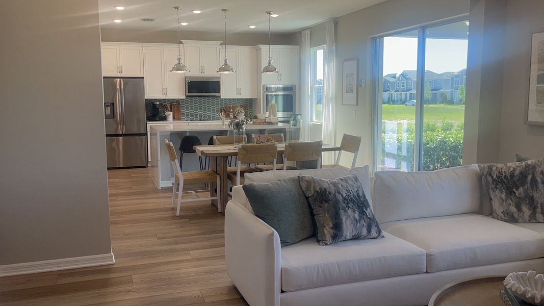 A modern open-concept living area with a sleek kitchen, dining table, and cozy white sofa, illuminated by natural light.