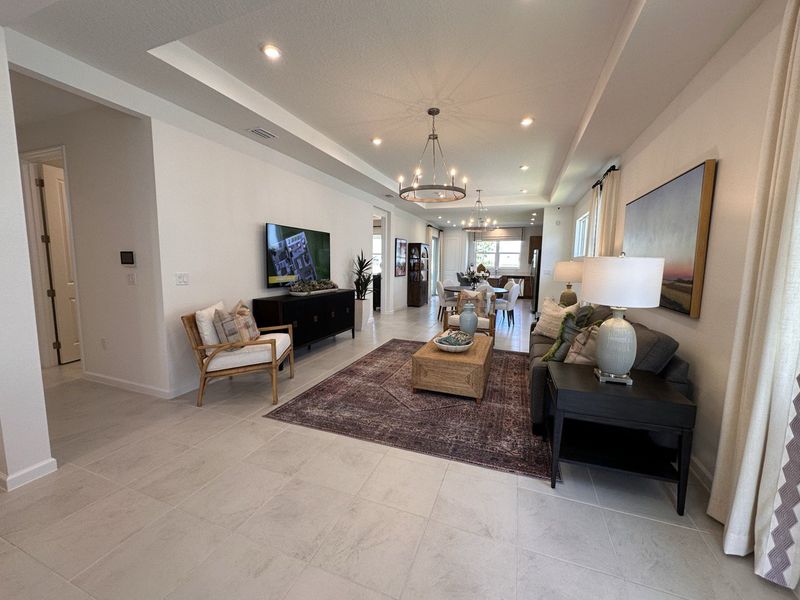 An elegant living room featuring cozy seating, a stylish chandelier, and modern decor leading to an open dining area.
