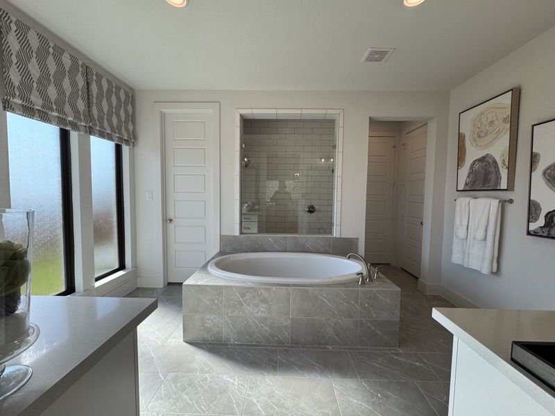 A luxurious bathroom featuring a central bathtub, modern tile, and elegant decor with abundant natural light.