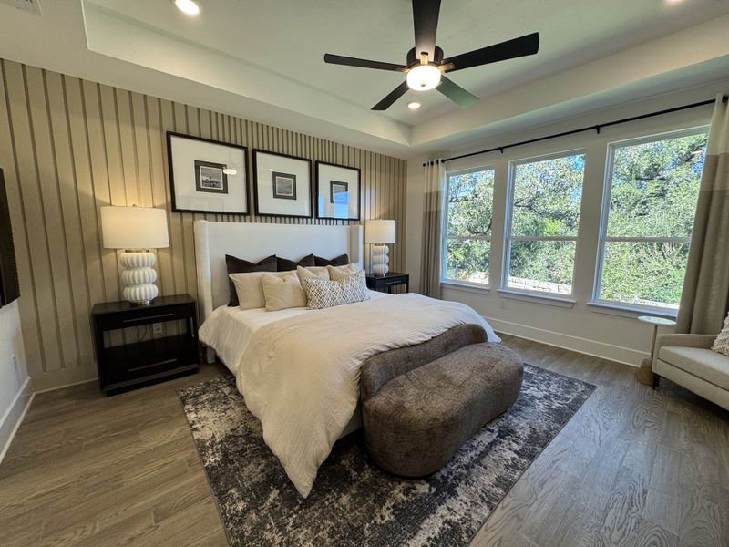 A cozy bedroom featuring a large bed, elegant lamps, and floor-to-ceiling windows with views of lush greenery.