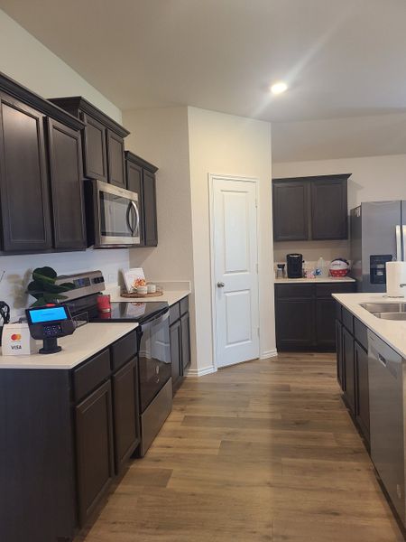 A modern kitchen with dark cabinets, stainless steel appliances, and sleek wood flooring.
