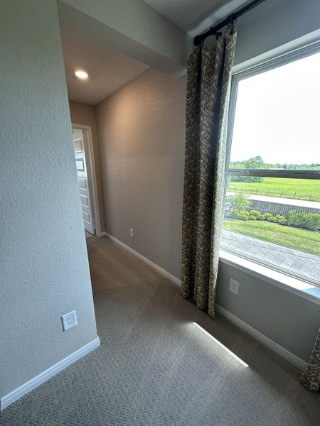 A cozy hallway with soft carpeting, patterned curtains, and a large window overlooking greenery.