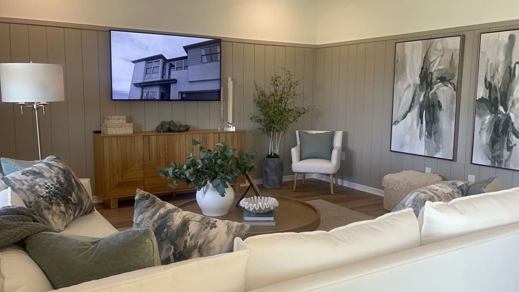 A cozy living room features neutral tones, plush seating, abstract art, and a large TV for a modern, inviting ambiance.