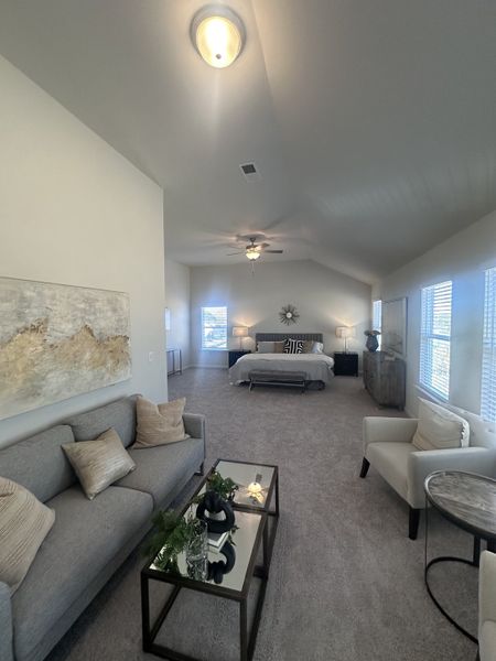 A spacious bedroom with plush carpet, cozy sitting area, modern art, and ample natural light from multiple windows.