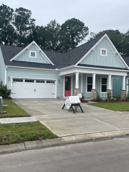 A charming light blue home with a welcoming porch and manicured lawn in Homecoming by True Homes (Ravenel, SC).