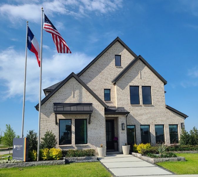 A beautiful beige brick home with a manicured lawn in Painted Tree - Woodland West by Normandy Homes (McKinney, TX).