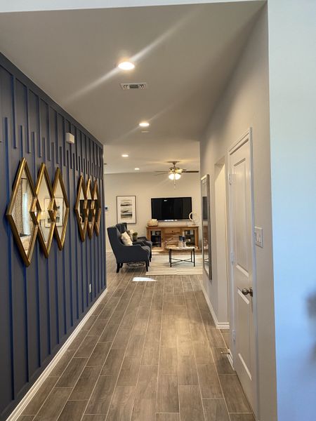 A modern hallway with wood-look tiles, blue accent wall, mirror decor, and cozy seating area leading to a living room.